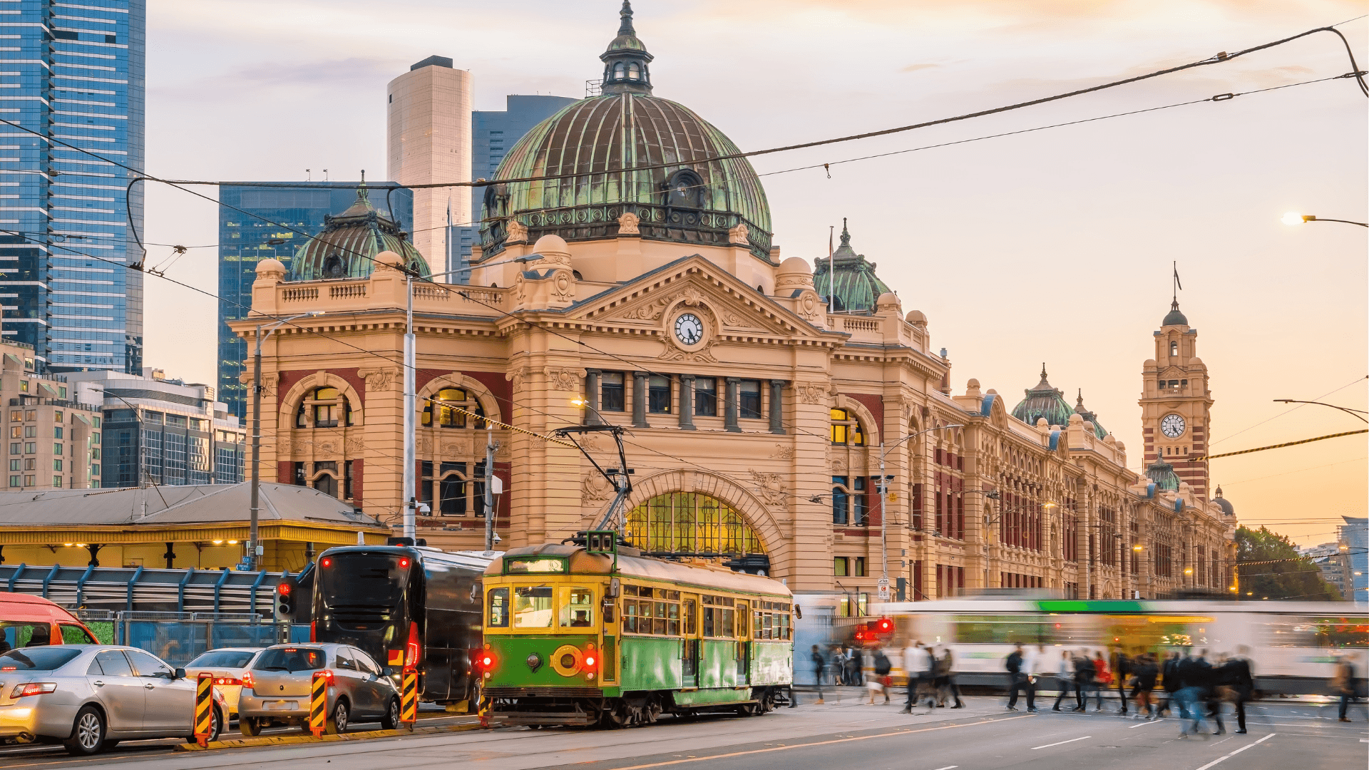the icon flinders street railway station in the background, melbourne city trams and traffic in the foreground, people crossing the street